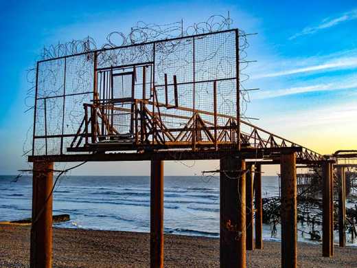 Photograph of barbed wire protected gate, part of Brighton's ruined West Pier. The pier was shut in 1975 after being deemed unsafe and then collapsed in the aftermath of Storm Imogen and finally burnt down in 2003.
