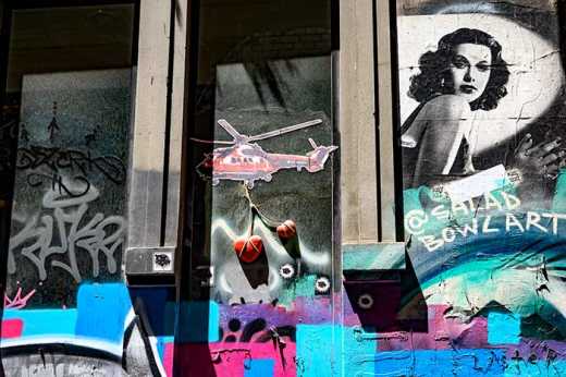 Photograph of stencil street art featuring helicopter with suspended 3D hearts.