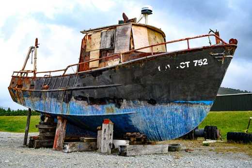 Photograph of old rusting boat in shipyard propped up by large wooden blocks.