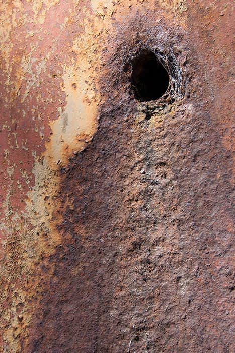 Photograph of heavily corroded metal plate (gold dredger hull).