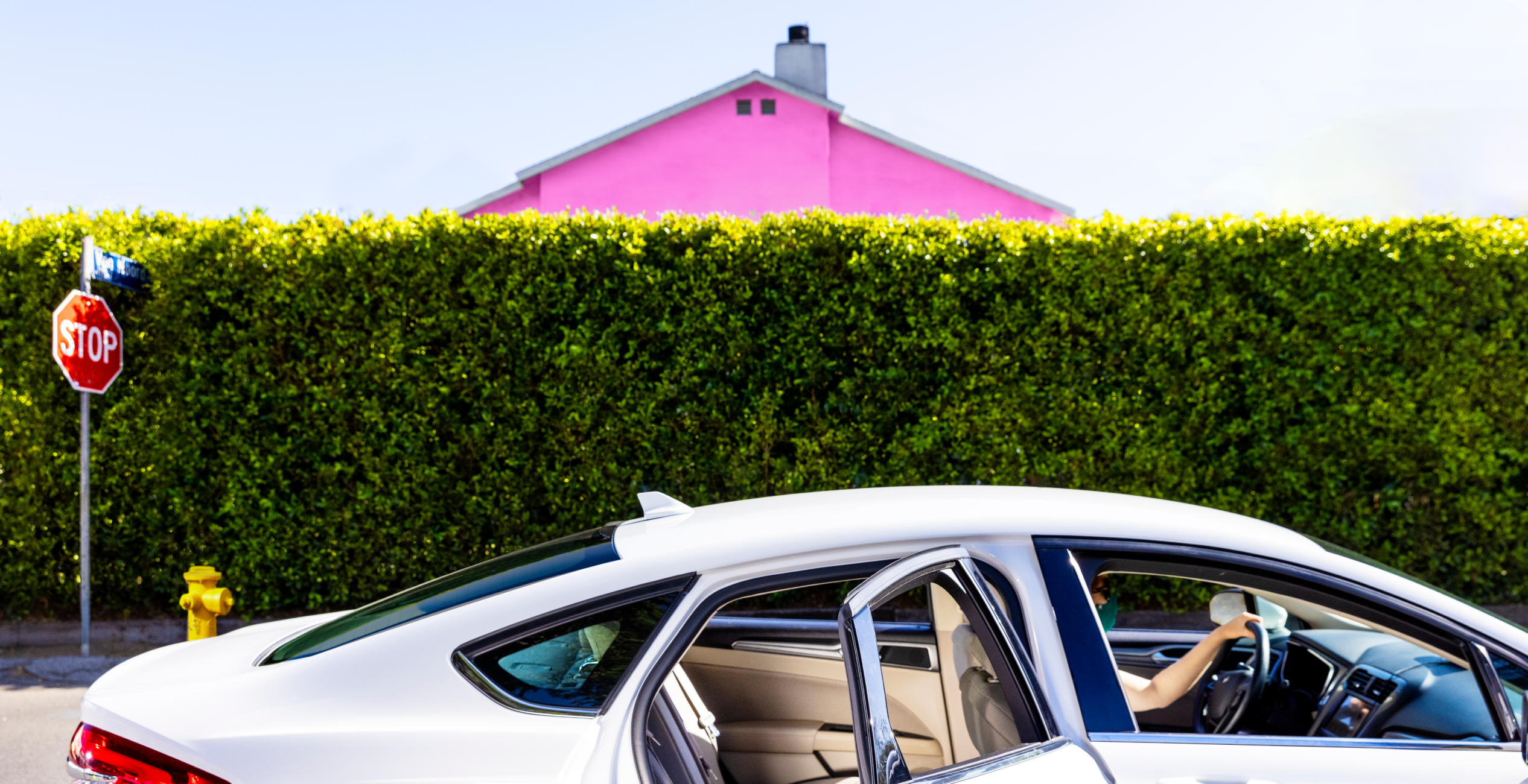 car with door open parked in front of hedges/bushes and pink house