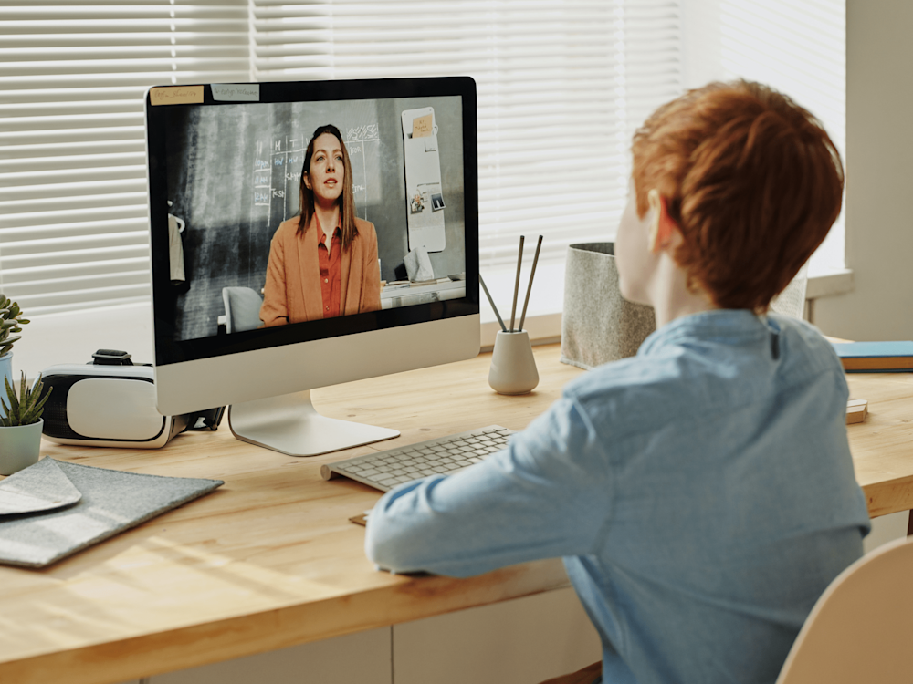 Young student at a desk watching virtual classroom video