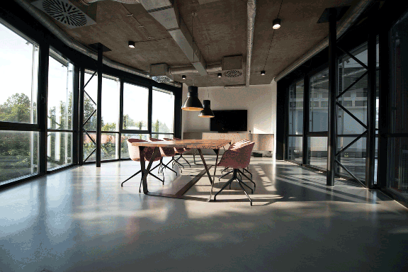 Empty open room with a table and chairs. One wall of the room in a window to the outside showing tress.