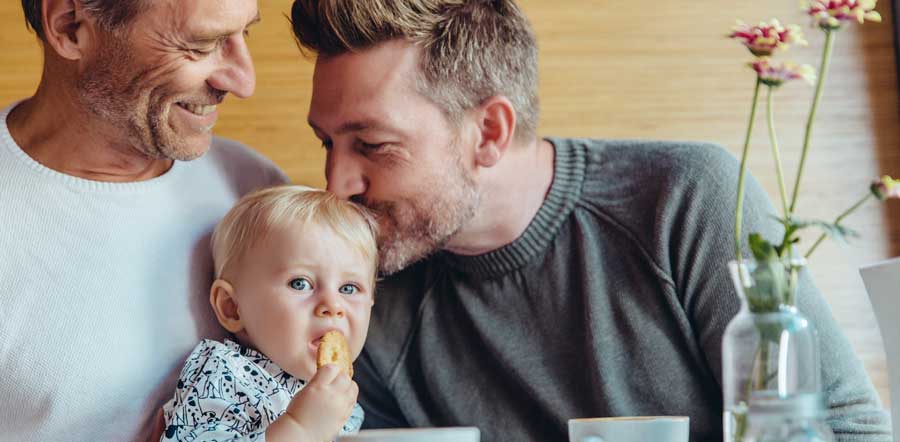 Baby being kissed by dads at breakfast table