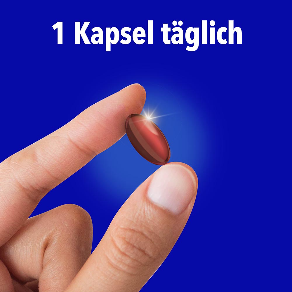 Hand hält eine rote Kapsel vor blauem Hintergrund mit dem Text „1 Kapsel täglich"
