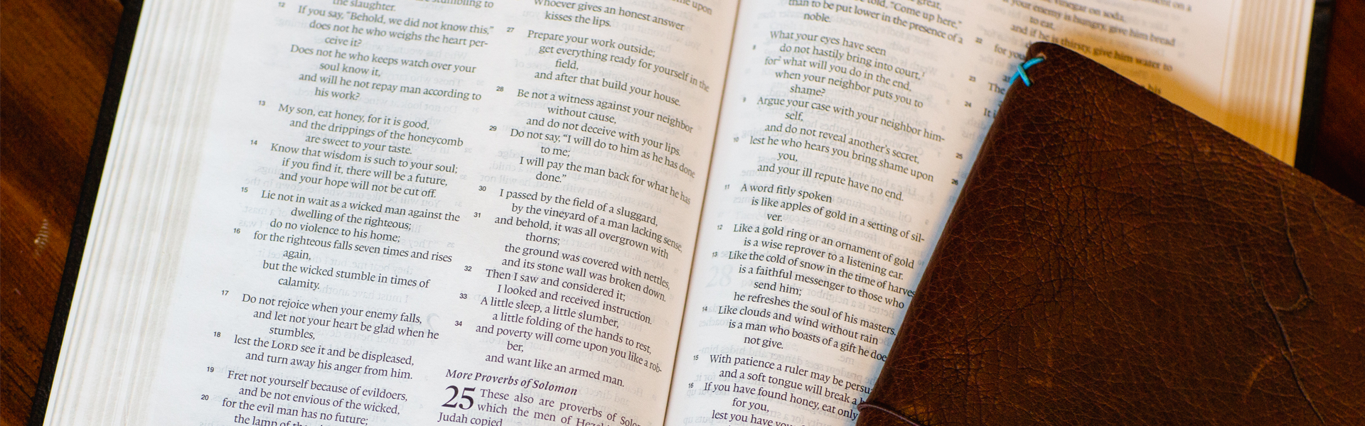 Open Bible displaying Proverbs with a leather journal on a wooden table symbolizing biblical wisdom, truth, and the foundation of faith for Watermark Resources’ Statement of Faith.