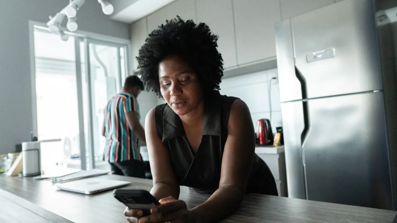 Woman in kitchen checking financial app for free cash advance