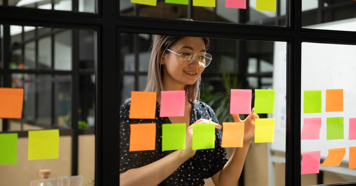 Asian business woman writes business processes on post it notes on glass wall