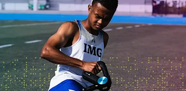IMG Academy athlete seated on the track using a recovery device, representing mental strength and resilience while overcoming injury.