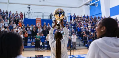 A student holds a trophy overhead in a crowded gymnasium.