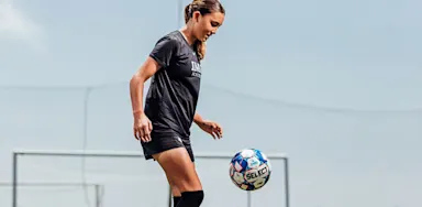 A soccer player controls a ball with her foot.