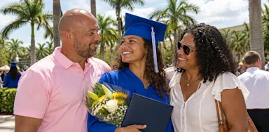 A graduate in a blue cap and gown smiles with her family.