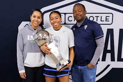 Championship winner (student-athlete) with trophy, flanked by two proud adults (coaches/parents), celebrating at the Chipotle Nationals basketball tournament.