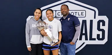 A student-athlete holds a trophy while posing with two adults.