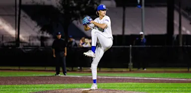 A baseball pitcher raises one knee during his delivery.