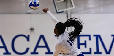 A volleyball player reaches overhead toward a ball during a game.