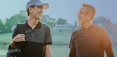 Young golfer walking alongside an older mentor on a golf course, smiling and talking, representing guidance, confidence, and intergenerational support in sports.