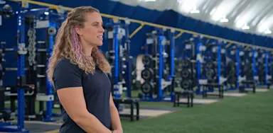 A trainer speaks in profile beside weight-training equipment.
