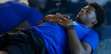 IMG Academy athlete lies on a gym floor with hands resting on their chest, eyes closed, practicing guided breathing or recovery during a training session.