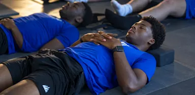 Athletes lie on mats with their hands resting on their chests during a relaxation exercise.