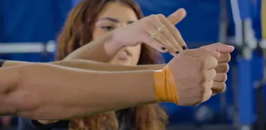 A trainer demonstrates an arm exercise with a resistance band around an athlete’s wrists.
