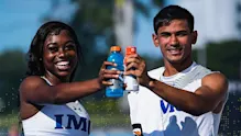 IMG Academy student-athletes smiling and clinking sports drink bottles on an outdoor field, celebrating hydration, teamwork, and recovery after training.