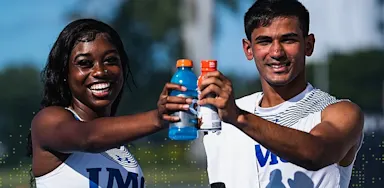 IMG Academy student-athletes smiling and clinking sports drink bottles on an outdoor field, celebrating hydration, teamwork, and recovery after training.