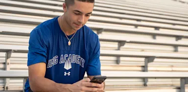 Student-athlete sitting in bleachers and using a smartphone, representing how athletes can engage with college recruiters through social media.