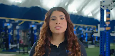 A trainer speaks to the camera in a weight room.