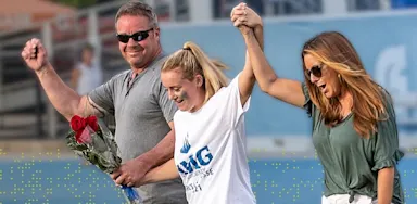 Parents walk hand in hand with their teenage athlete on a sports field, celebrating together and illustrating positive parent involvement.