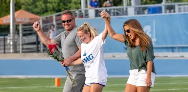 A student-athlete celebrates with two adults, holding their hands aloft.