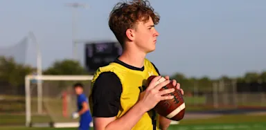 A quarterback holds a football with both hands while looking downfield.