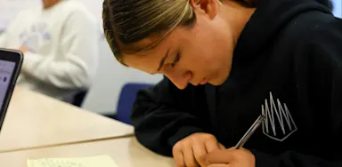 Student-athlete wearing a black sweatshirt taking notes or journaling on yellow paper reflecting on past athletic performance.