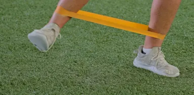 A close view shows an athlete balancing with a resistance band around the ankles.