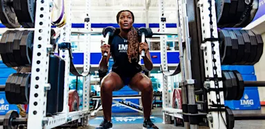 Female athlete performing a squat using a safety squat bar inside a weight room power rack.