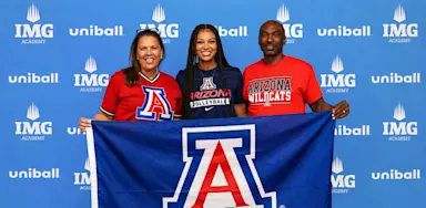 A student-athlete poses with two family members holding a University of Arizona banner at a signing event.
