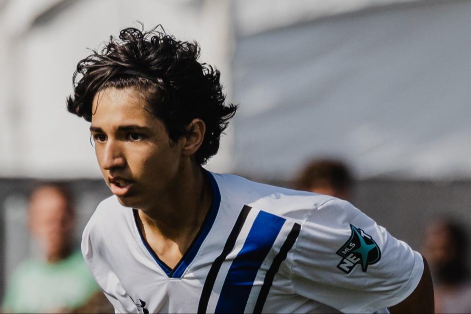 Focused male soccer player running during a match, wearing a white and blue uniform.