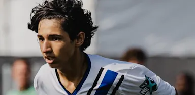 Focused male soccer player running during a match, wearing a white and blue uniform.