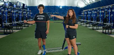 A trainer guides an athlete through a resistance-band shoulder exercise.