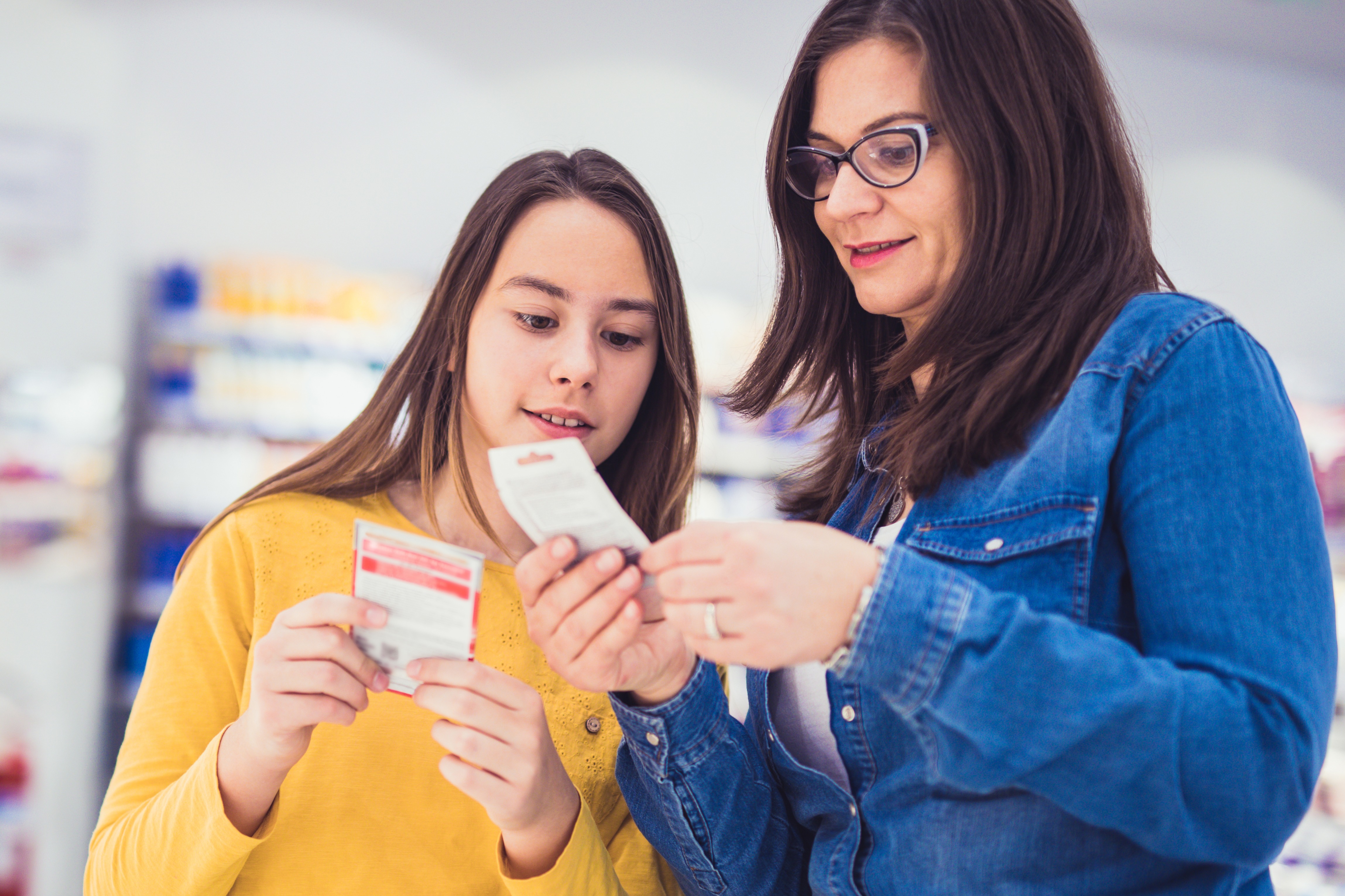Mother and teenage daughter in a store aisle reading a product label or supplement information, emphasizing parental guidance in nutrition.