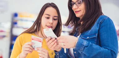 Mother and teenage daughter in a store aisle reading a product label or supplement information, emphasizing parental guidance in nutrition.