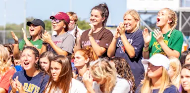 Group of student-athletes enthusiastically cheering and wearing college gear, representing the excitement and strong community often found in junior college athletic programs.