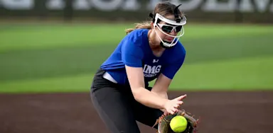 A softball player fields a ball while wearing a protective face mask.