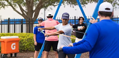 A coach leads athletes through a resistance-band exercise outdoors.