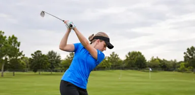 A golfer follows through on a swing on a course.