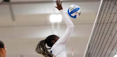 A volleyball player reaches up to strike the ball beside the net.