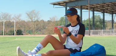 A seated athlete eats a slice of watermelon beside a sports bag.