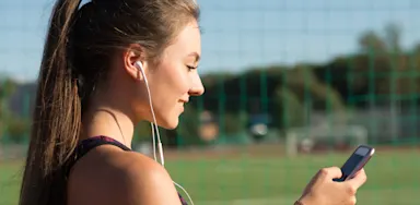 An athlete looks at her phone beside a sports field.