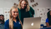 Student-athlete researching colleges on a laptop with guidance from a teacher, illustrating the support available during the college search process.