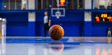 A basketball rests on the floor of an empty indoor court.